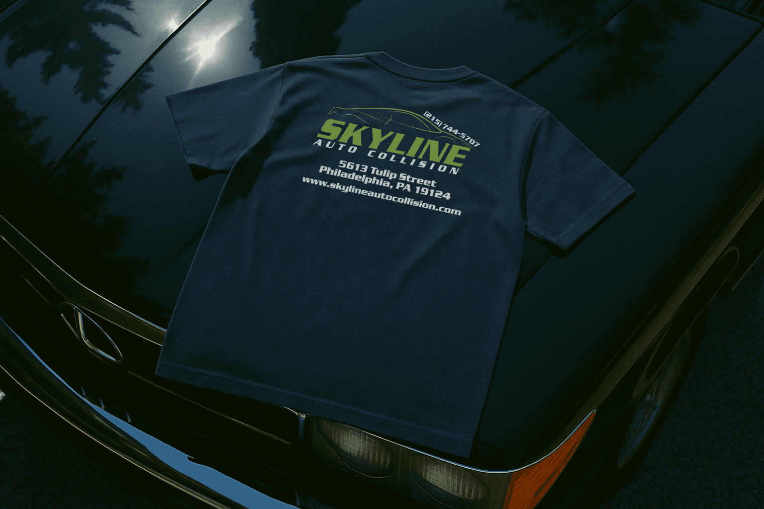 How can shirts tell your brand's story in the automotive industry? Skyline Auto Collision branded t‑shirt displayed on a car hood, highlighting logo placement and professional image.