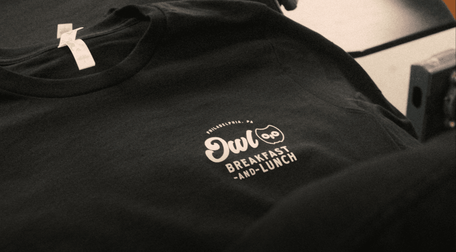 Rob Kang Owl Breakfast black t-shirt with owl logo and Philadelphia, PA design, used as restaurant merchandise and uniforms.