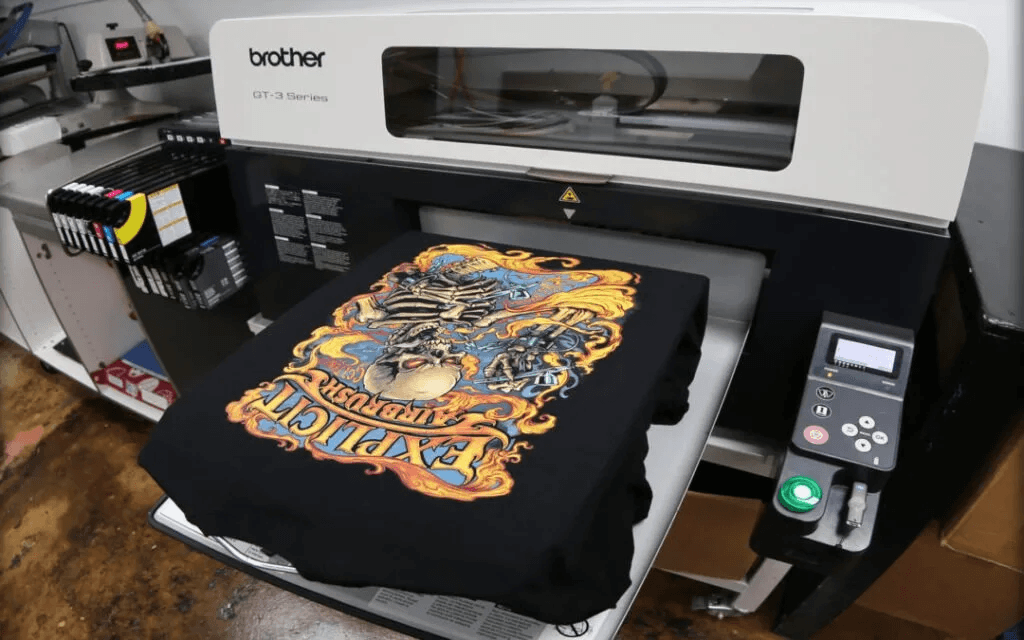 A Brother GT-3 Series DTG printer producing a detailed, full-color design on a black t-shirt, demonstrating the precision and creative potential of DTG printing—ideal for illustrating what is DTG printing in a professional apparel setting.