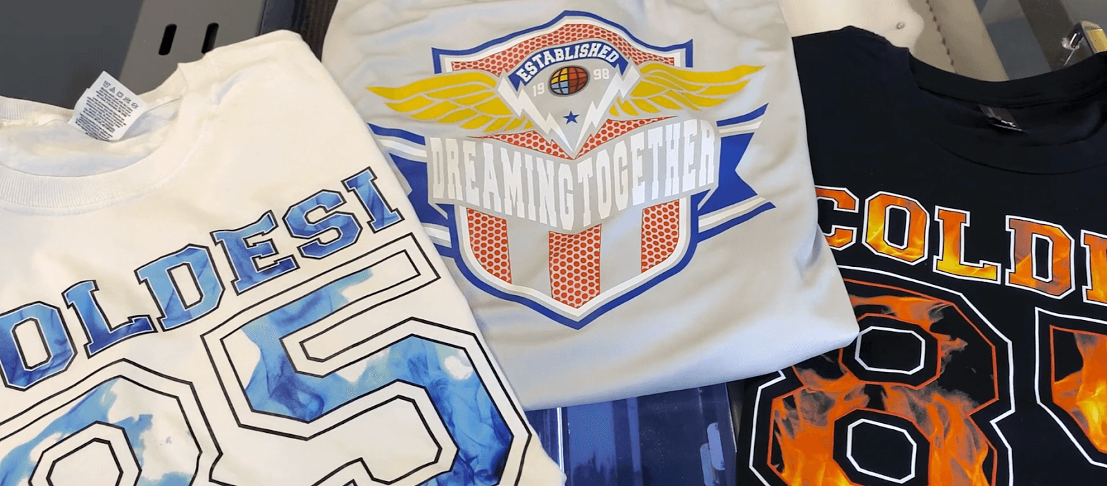 Three DTG printed t-shirts featuring bold graphics and text, showcasing the design versatility and color vibrancy achievable with DTG technology—an eye-catching example for those asking what is DTG printing and what results to expect.