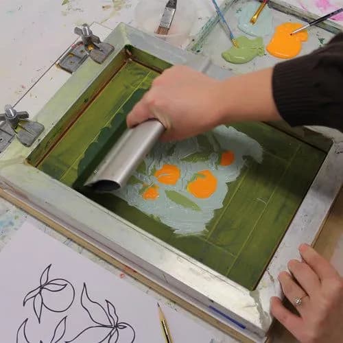 The process of silk screen printing t shirts, with an artist pulling ink over a stencil from a t shirt design drawing.