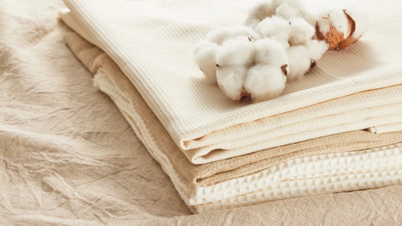 Stack of natural cotton fabrics with cotton bolls, ideal for custom t-shirt design and apparel making.