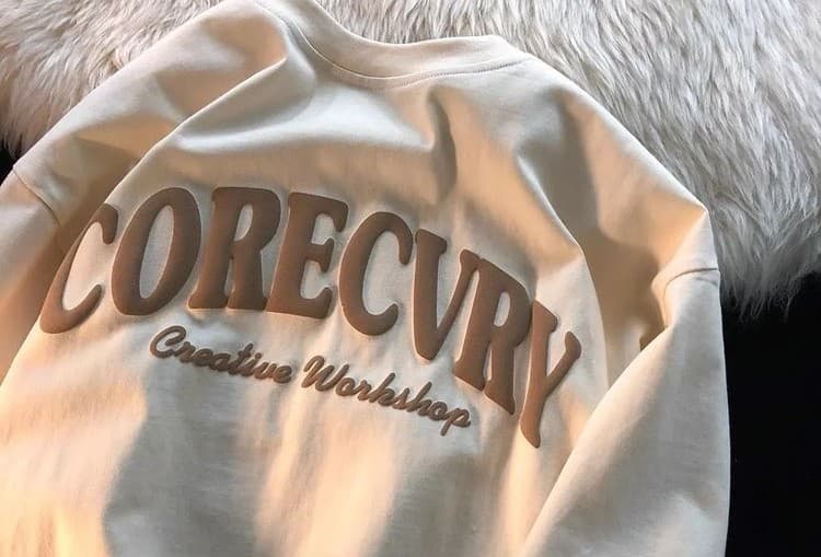 A cream sweatshirt with bold raised “CORECVRY” lettering showcases what is puff printing in streetwear design. The textured ink printing demonstrates puff ink screen printing, where custom puff printing creates a premium, tactile effect that elevates apparel branding.