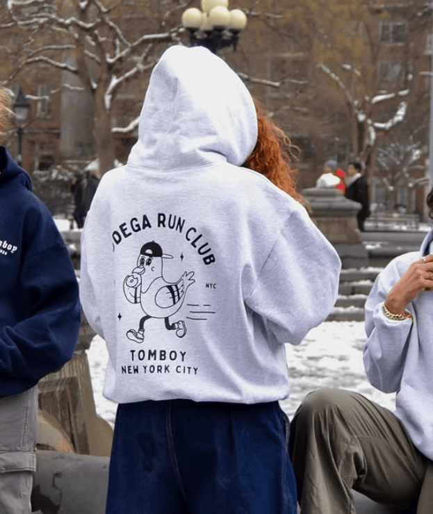Tomboy Athletic Club hoodie with Bodega Run Club graphic worn in snowy New York City park, showcasing bold streetwear design and brand identity.